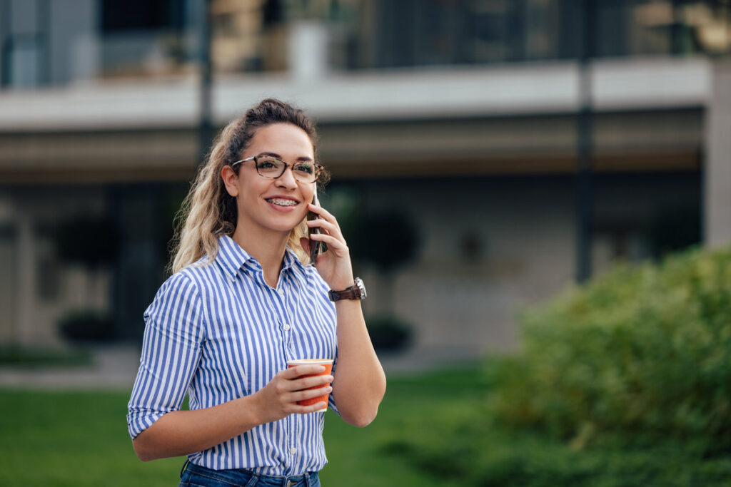 Smiling girl talking with someone over the phone, holding a cup of coffee.