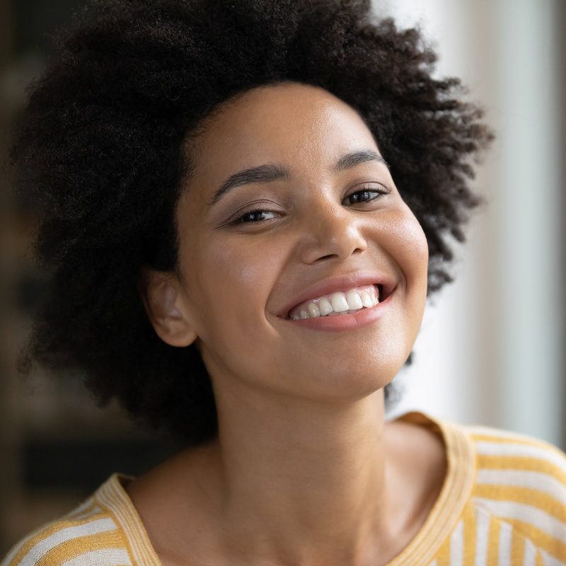 Head shot happy beautiful african american woman looking at camera. Joyful millennial mixed race female client with white toothy smile and perfect skin satisfied with dentistry or cosmetology service.