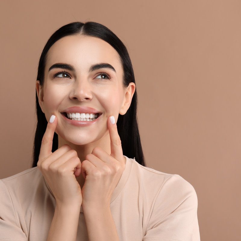 Beautiful woman showing her clean teeth and smiling on beige background, space for text