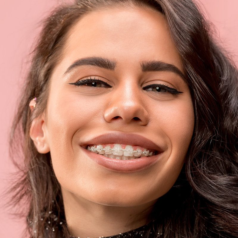 Beautiful young woman with teeth braces on pink