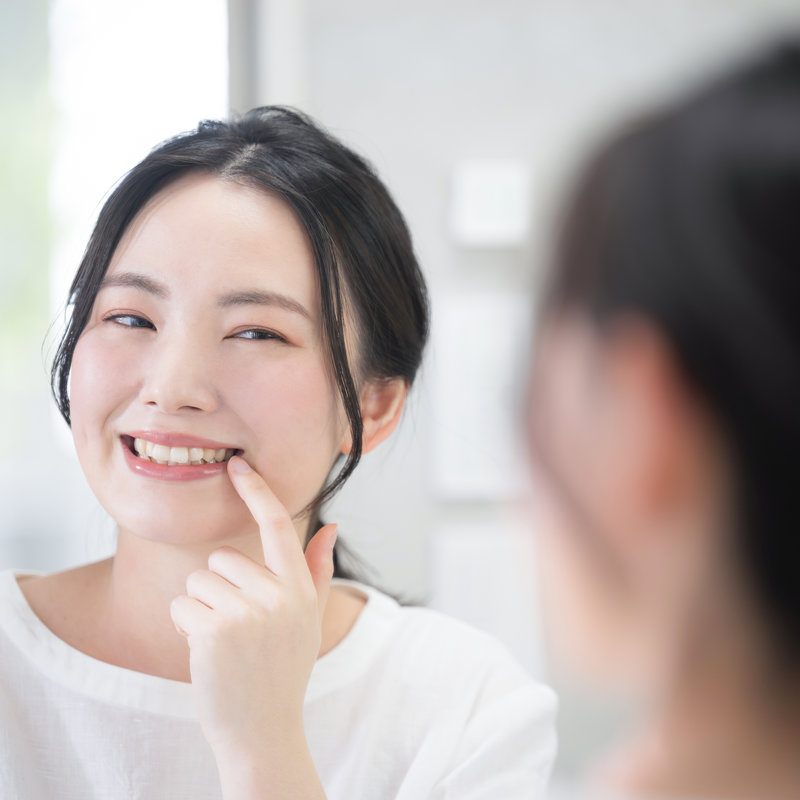 Cute woman looking at her teeth and whiteness while looking in the mirror whitening, etc. Close up
