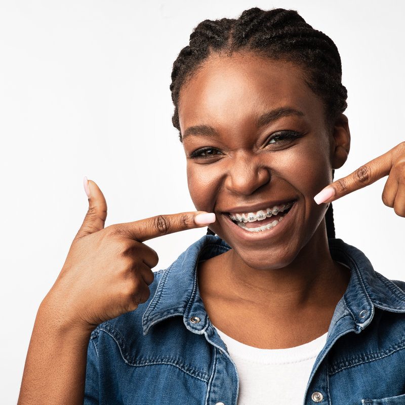 Girl smiling pointing fingers at brackets on teeth, studio shot