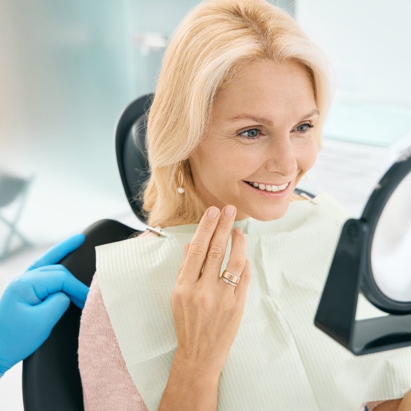 Happy smiling woman is looking to the mirror in dental chair