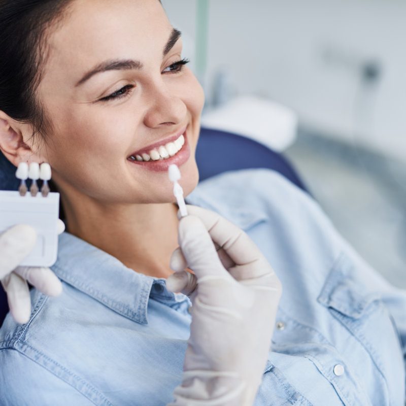 Male dentist comparing color of lady teeth with sample