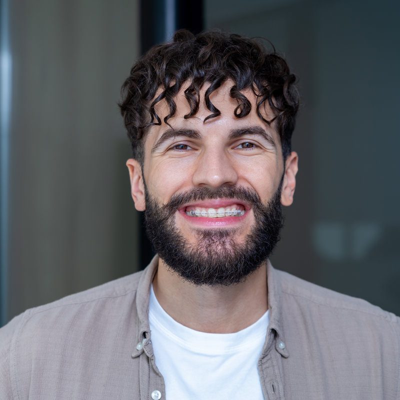 Man with cheerful smile showing clear ceramic braces on his teeth after dentist visit