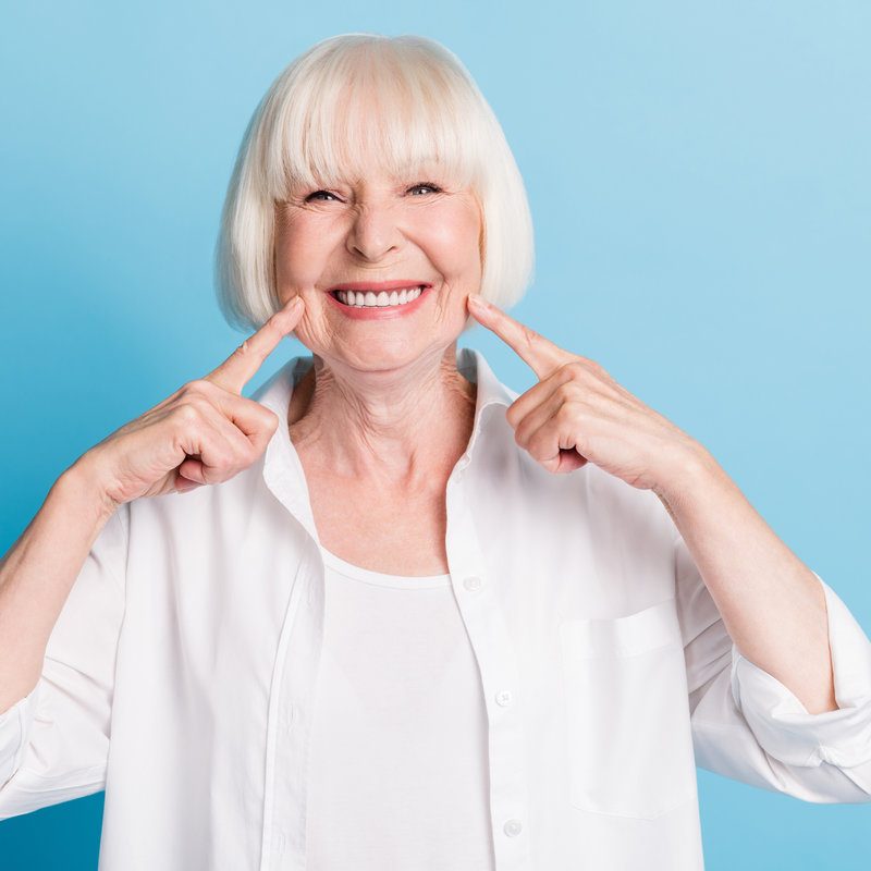 Photo portrait of granny blonde hair pointing at white teeth healthy smile dental whitening veneers isolated on bright blue color background