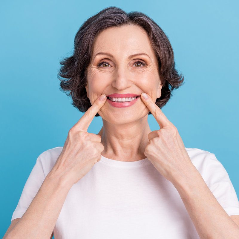 Photo portrait woman smiling showing finger pointing white teeth veneers isolated pastel blue color background