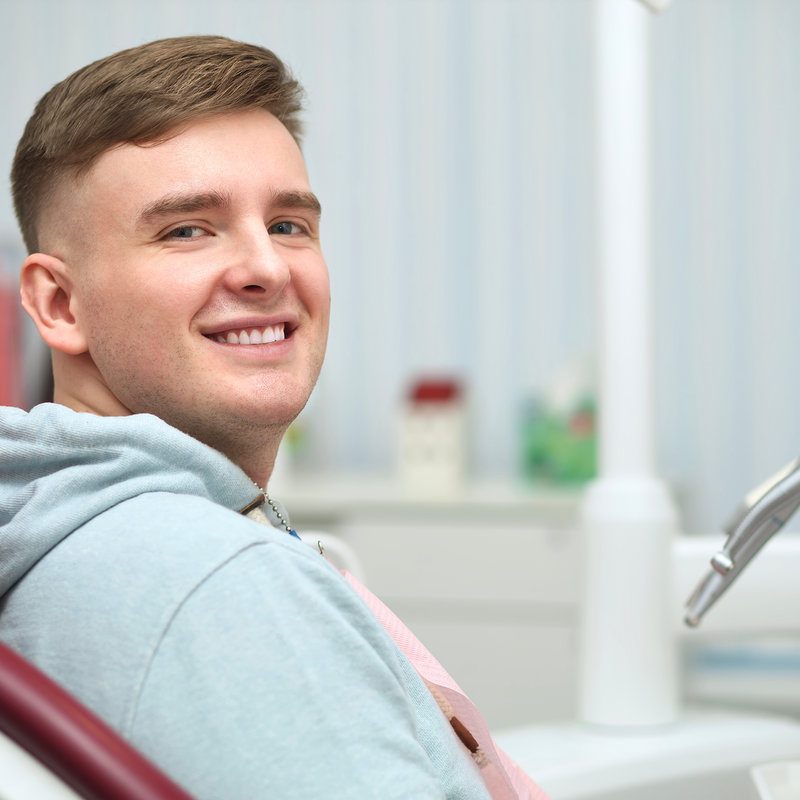 Portrait of happy satisfied smiling with white teeth young man patient with perfect smile, positive guy having a seat, sitting on dentist medical chair in dental office after treatment in clinic