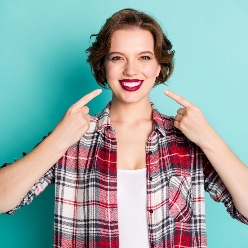 Portrait of positive cheerful girl point index finger on beaming smile show her perfect ideal teeth after medicine clinic wear stylish clothing isolated over teal color background
