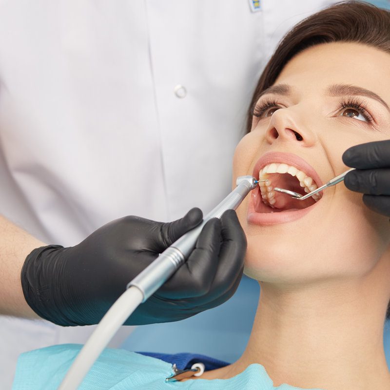 Young female patient visiting dentist office. Beautiful woman with healthy straight white teeth sitting at dental chair with open mouth during a dental procedure. Dental clinic. Stomatology.