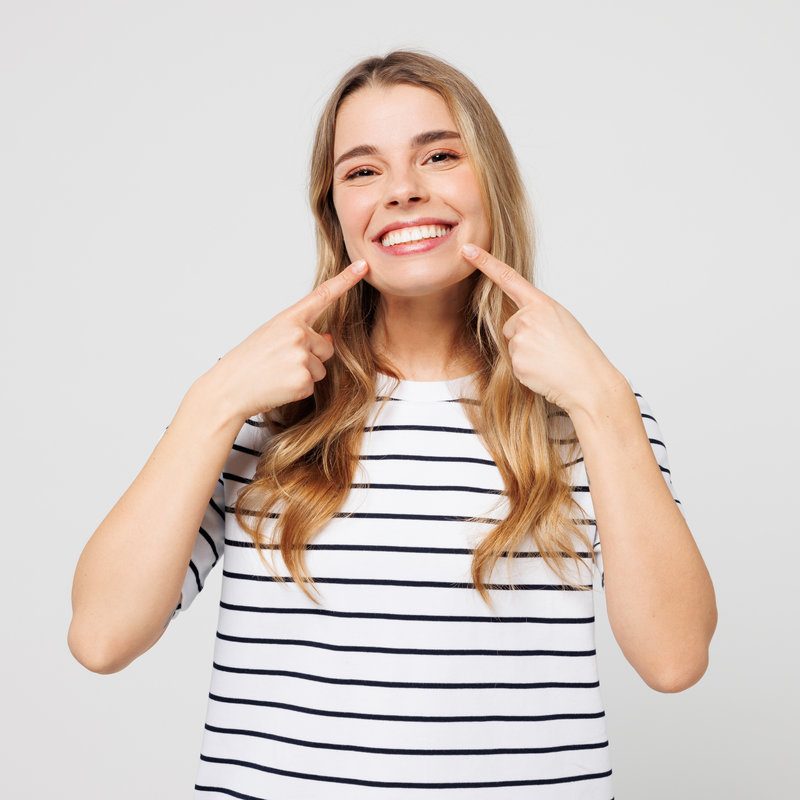 Young happy smiling caucasian cheerful woman wear striped t shirt casual clothes point index fingers on opened mouth teeth isolated on plain solid white background studio portrait. Lifestyle concept.