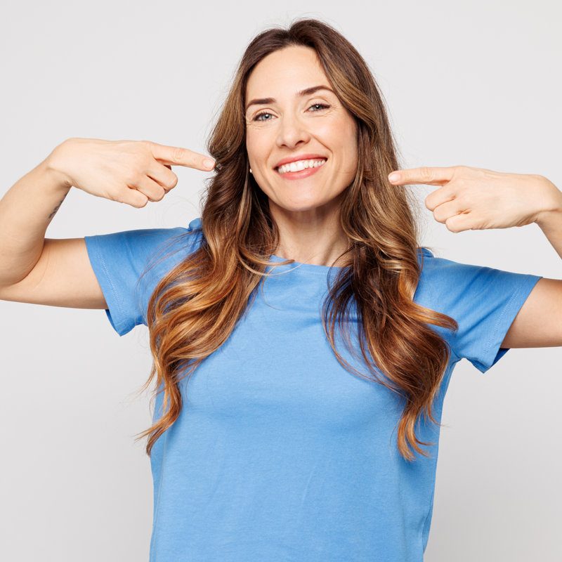Young smiling caucasian woman wears blue t shirt casual clothes point index fingers on opened mouth teeth look camera isolated on plain solid white color background studio portrait. Lifestyle concept